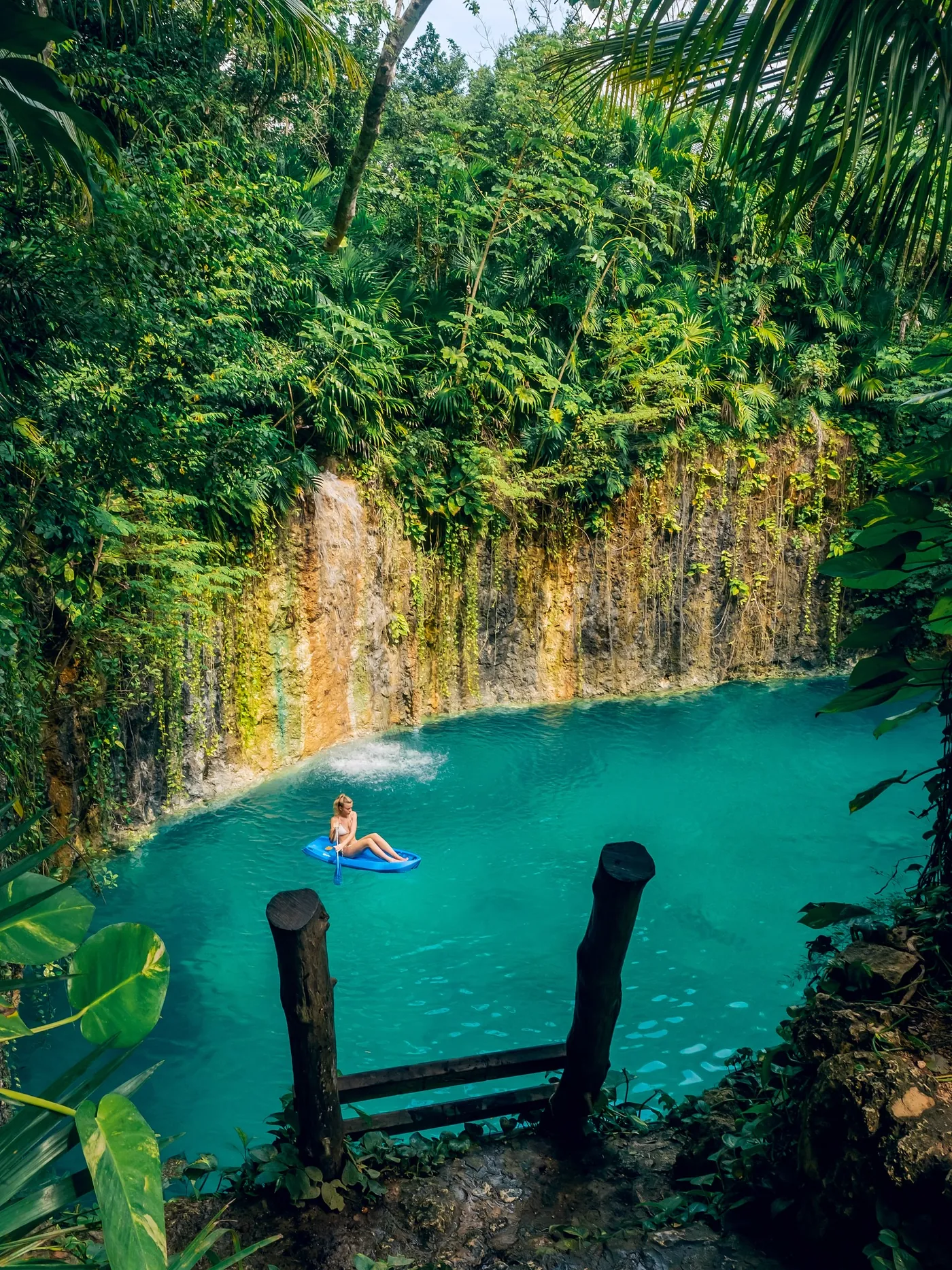 Una persona flota en el cenote turquesa de Atik bajo una pared de roca con cascada