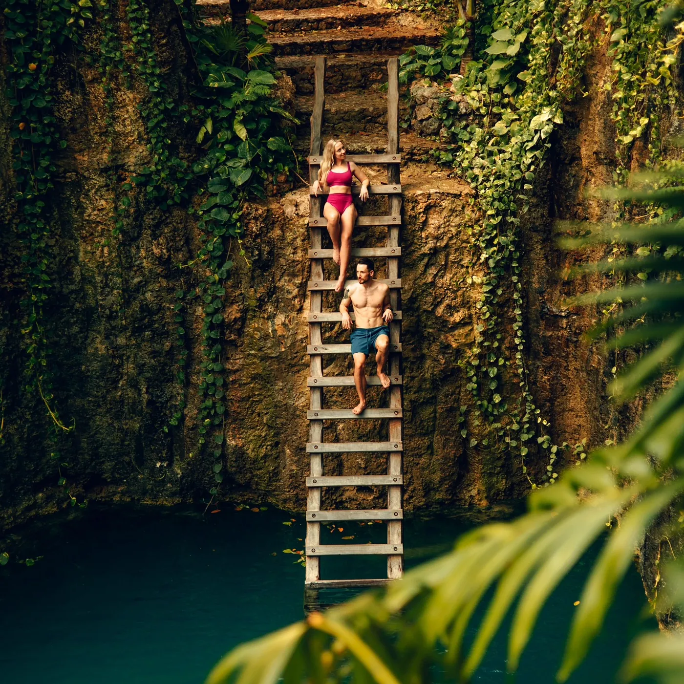 Dos visitantes bajan una escalera de madera por la pared del cenote