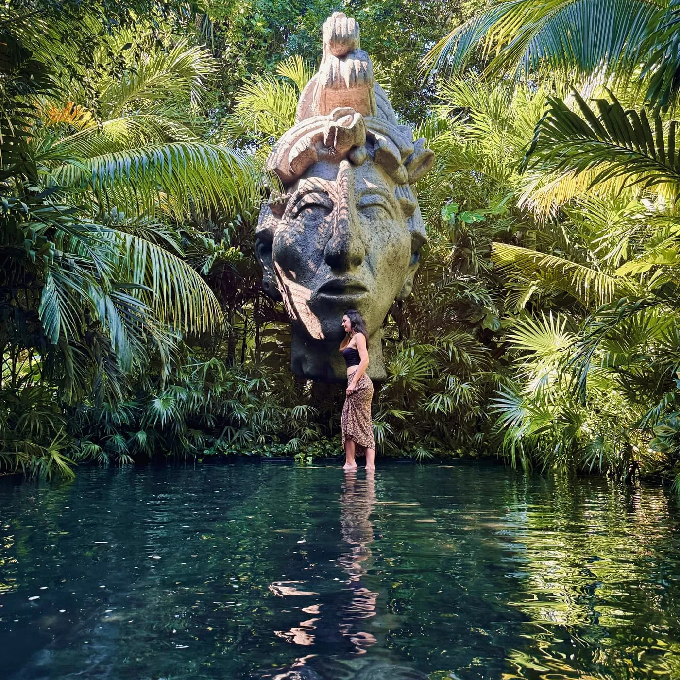 Una escultura de rostros apilados se alza sobre una alberca en la selva